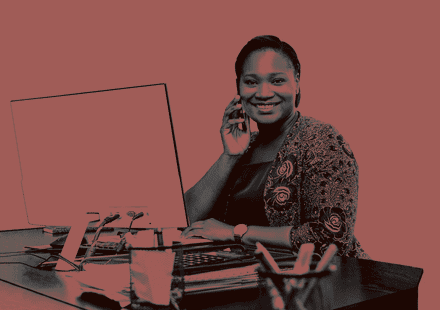 A smiling school administrator at her desk holding a phone to her ear